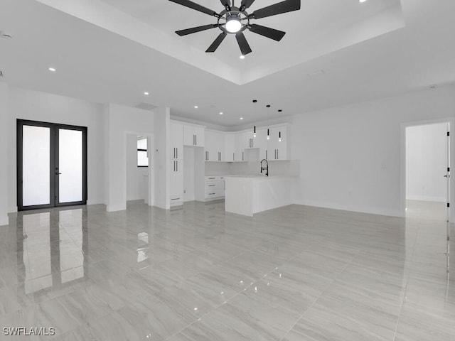 unfurnished living room with french doors, ceiling fan, a tray ceiling, and sink