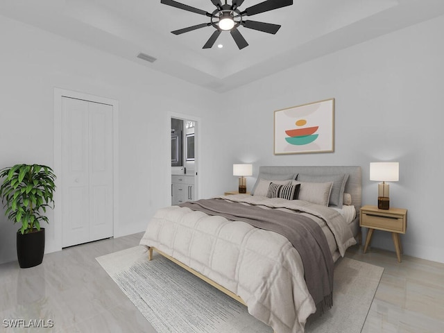 bedroom featuring ceiling fan, connected bathroom, and a tray ceiling