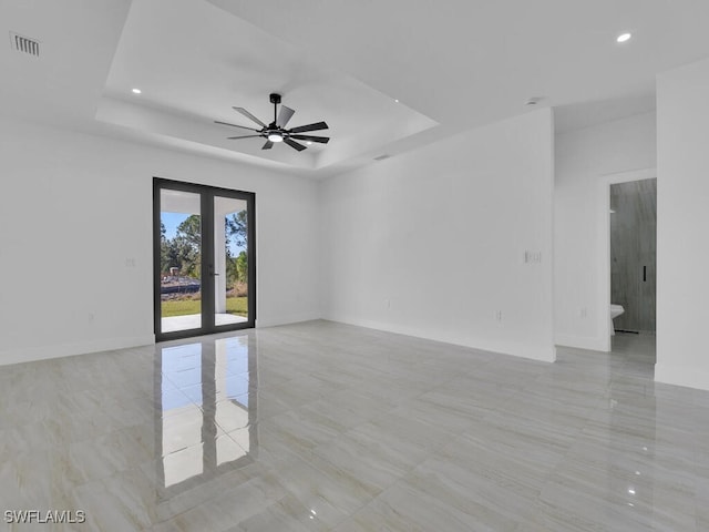 empty room with a raised ceiling, ceiling fan, and french doors