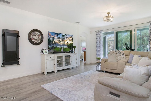 living area featuring baseboards, arched walkways, visible vents, and light wood-style floors