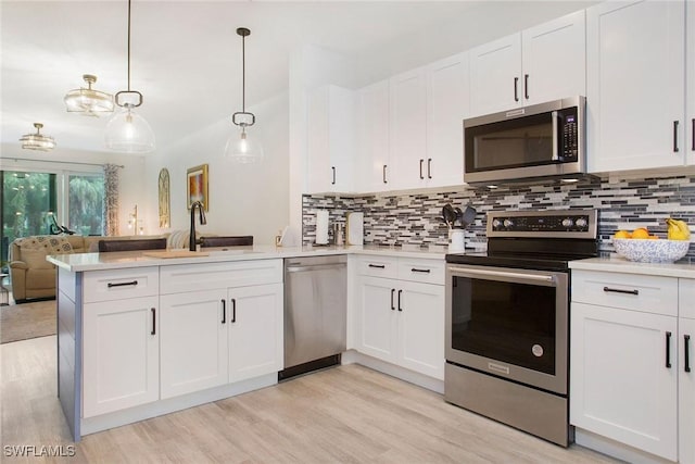 kitchen with a sink, white cabinetry, light countertops, appliances with stainless steel finishes, and hanging light fixtures