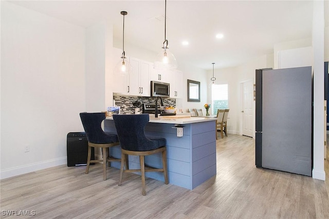 kitchen with tasteful backsplash, appliances with stainless steel finishes, decorative light fixtures, light countertops, and white cabinetry