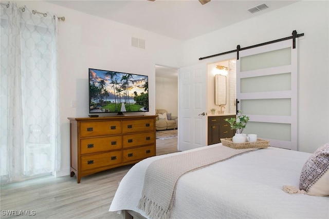 bedroom featuring a barn door, connected bathroom, and light wood-type flooring