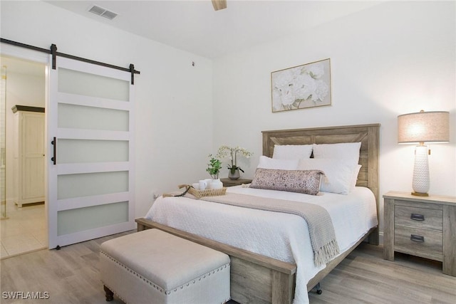 bedroom with ceiling fan, a barn door, and light hardwood / wood-style flooring