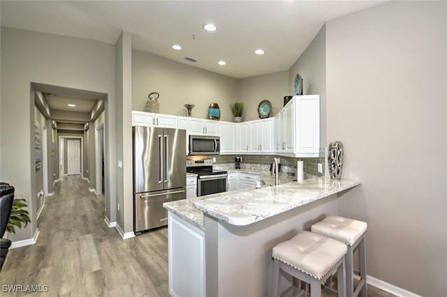 kitchen with backsplash, white cabinets, a kitchen bar, kitchen peninsula, and stainless steel appliances