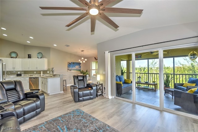 living room featuring ceiling fan with notable chandelier, sink, light hardwood / wood-style floors, and vaulted ceiling