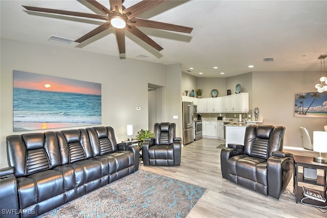 living room featuring ceiling fan with notable chandelier, sink, and light hardwood / wood-style floors