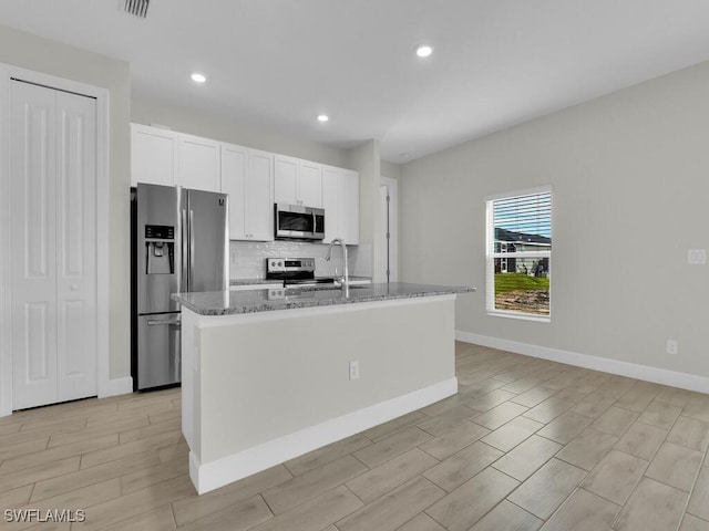 kitchen featuring appliances with stainless steel finishes, stone countertops, an island with sink, sink, and white cabinets