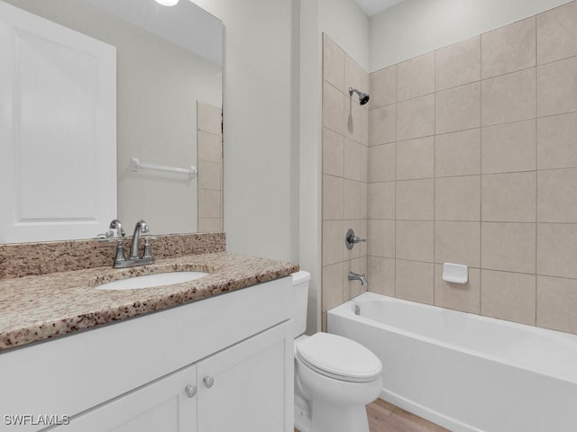 full bathroom featuring vanity, hardwood / wood-style floors, tiled shower / bath combo, and toilet