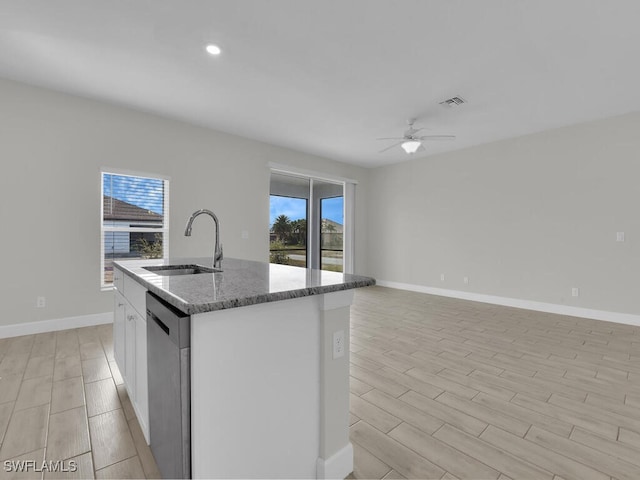 kitchen featuring sink, dishwasher, white cabinetry, a kitchen island with sink, and dark stone countertops