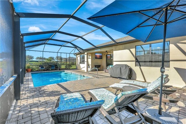 view of pool with ceiling fan, grilling area, a patio, and glass enclosure