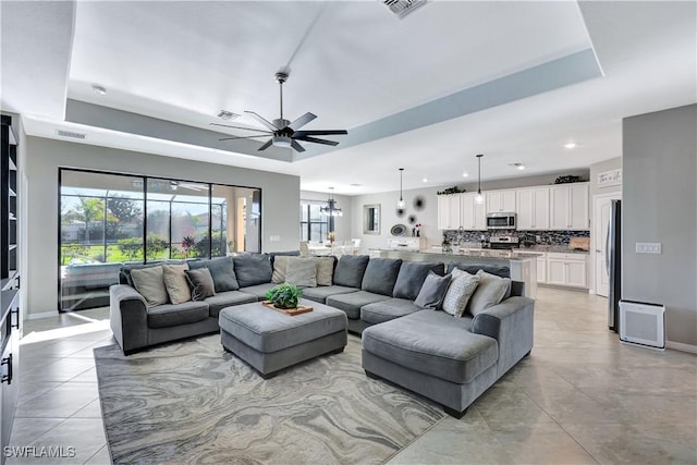 living room with light tile patterned floors, a tray ceiling, and ceiling fan with notable chandelier