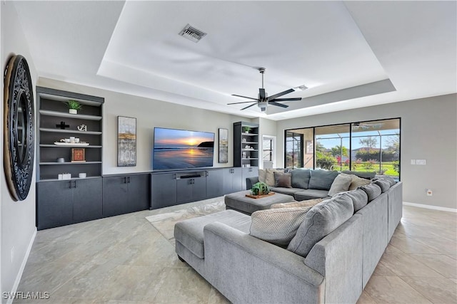 living room featuring light tile patterned floors, built in features, ceiling fan, and a tray ceiling