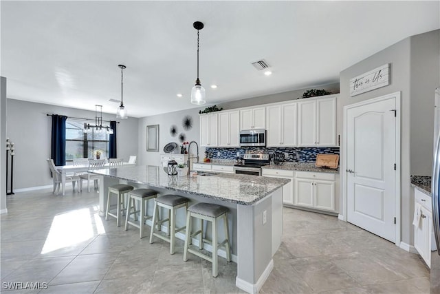 kitchen featuring appliances with stainless steel finishes, pendant lighting, white cabinetry, sink, and a kitchen island with sink