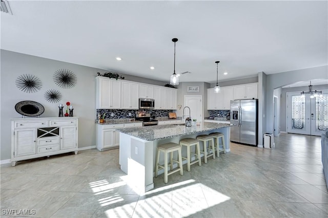 kitchen featuring sink, a kitchen island with sink, stainless steel appliances, white cabinets, and a kitchen bar