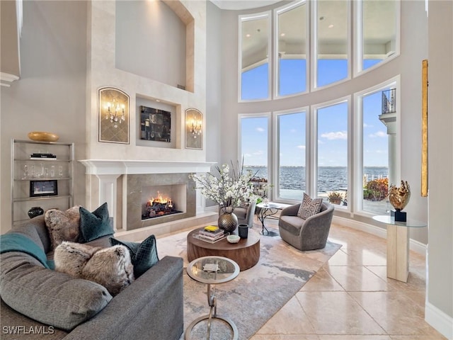 living room with a fireplace, light tile patterned flooring, a high ceiling, and a water view