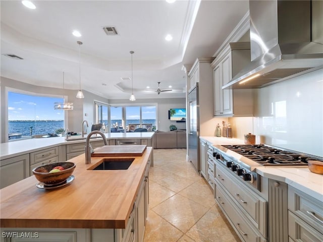 kitchen featuring wood counters, wall chimney range hood, a kitchen island with sink, and sink