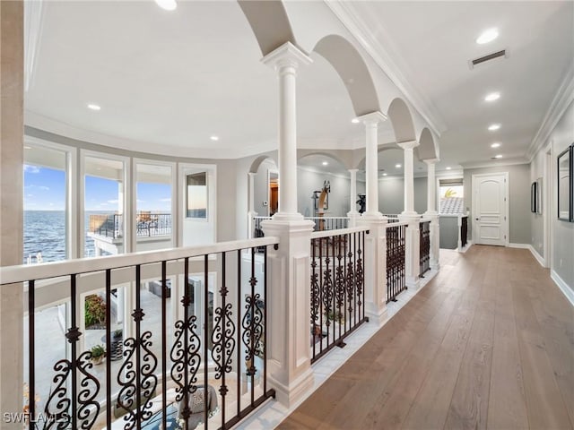 corridor with a water view, crown molding, decorative columns, and hardwood / wood-style flooring