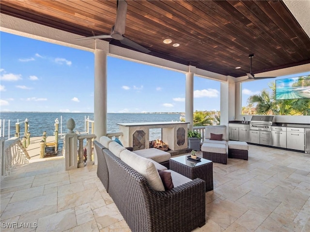 view of patio / terrace with ceiling fan, an outdoor living space with a fireplace, a water view, area for grilling, and exterior kitchen