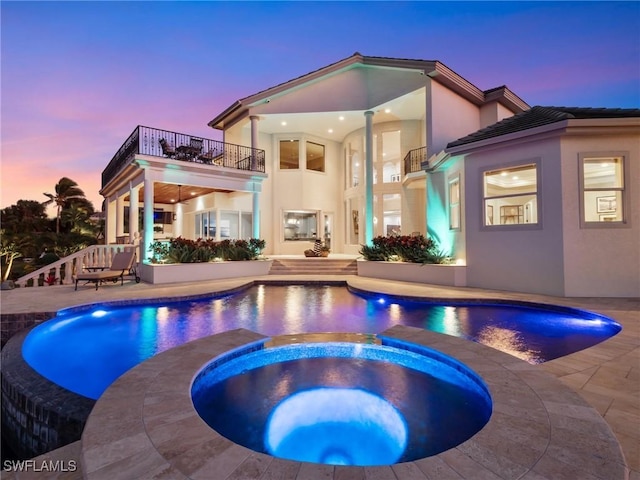 pool at dusk with an in ground hot tub and a patio area