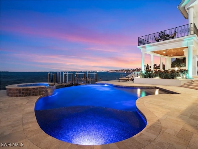 pool at dusk featuring an in ground hot tub, a water view, and a patio area