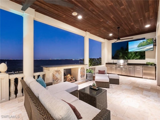 patio terrace at dusk with a water view, an outdoor living space with a fireplace, exterior kitchen, and sink