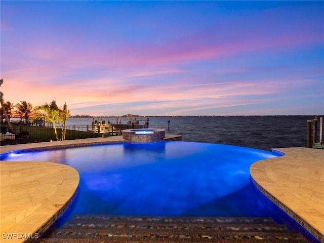 pool at dusk with an in ground hot tub, a water view, and a patio area