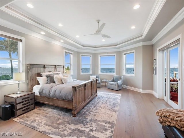 bedroom featuring crown molding, a tray ceiling, light wood-type flooring, and a water view