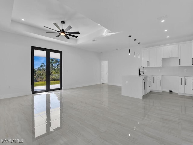 unfurnished living room featuring french doors, sink, ceiling fan, and a tray ceiling