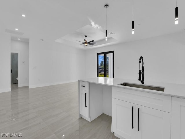 kitchen with pendant lighting, sink, ceiling fan, a tray ceiling, and white cabinets