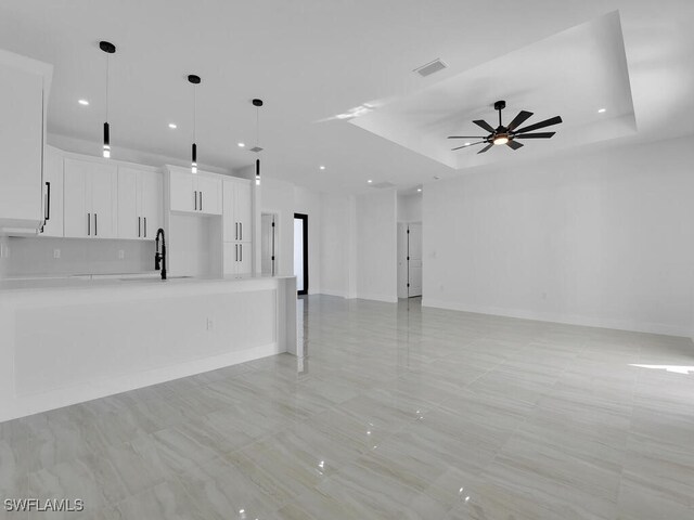 unfurnished living room with sink, a raised ceiling, and ceiling fan