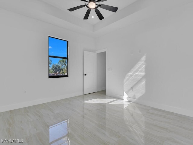 empty room with a high ceiling, ceiling fan, and a tray ceiling