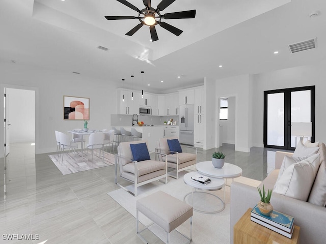 living room with french doors, ceiling fan, a tray ceiling, and sink