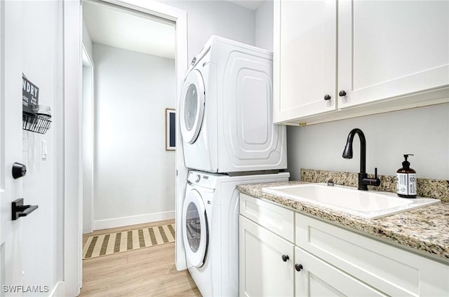 washroom featuring cabinets, stacked washing maching and dryer, sink, and light hardwood / wood-style floors