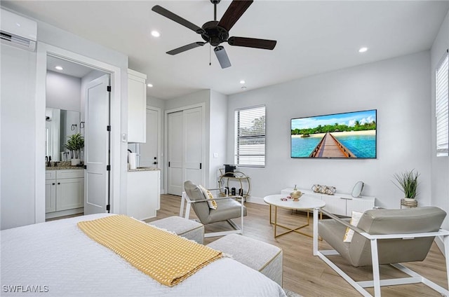 bedroom featuring light hardwood / wood-style flooring, ceiling fan, a wall mounted AC, ensuite bathroom, and a closet