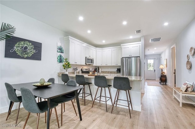 kitchen with appliances with stainless steel finishes, light hardwood / wood-style floors, light stone countertops, white cabinets, and kitchen peninsula