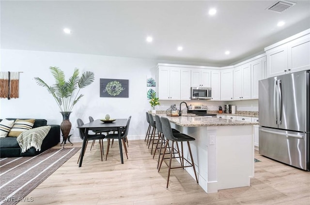 kitchen with light stone countertops, appliances with stainless steel finishes, a breakfast bar, and white cabinets