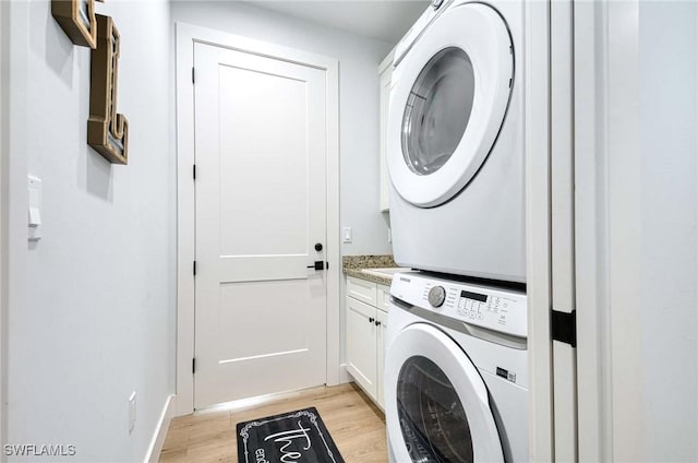 clothes washing area with cabinets, stacked washer / dryer, and light hardwood / wood-style flooring