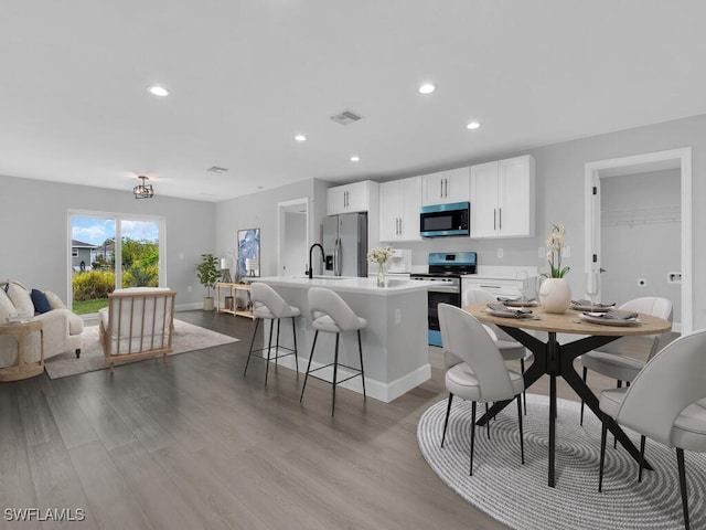 kitchen featuring a breakfast bar, appliances with stainless steel finishes, an island with sink, white cabinets, and light wood-type flooring