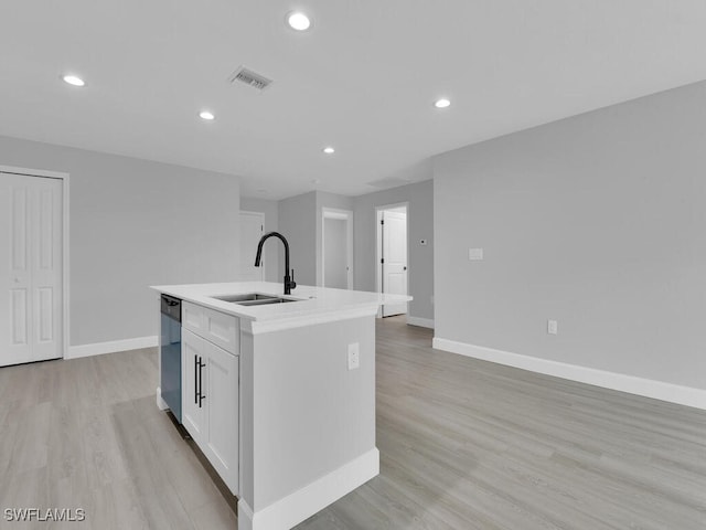 kitchen featuring an island with sink, black dishwasher, sink, white cabinets, and light wood-type flooring