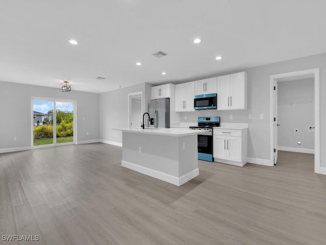 kitchen featuring stainless steel appliances, an island with sink, light wood-type flooring, and white cabinetry