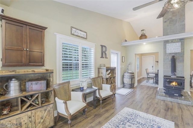 living area featuring lofted ceiling, hardwood / wood-style flooring, ceiling fan, and a wood stove