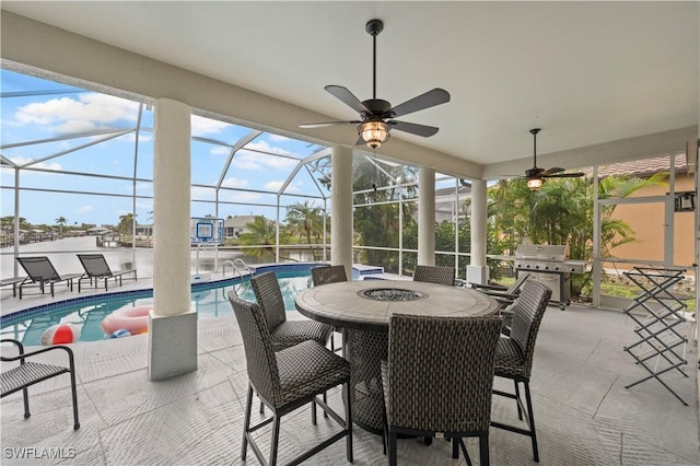 view of patio with ceiling fan, area for grilling, and glass enclosure