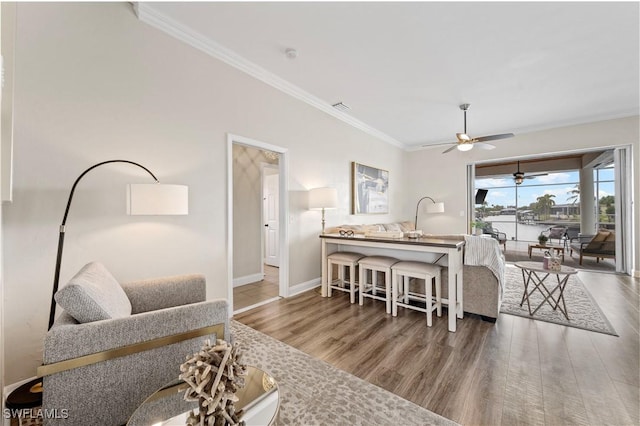 living area featuring a ceiling fan, visible vents, baseboards, ornamental molding, and wood finished floors