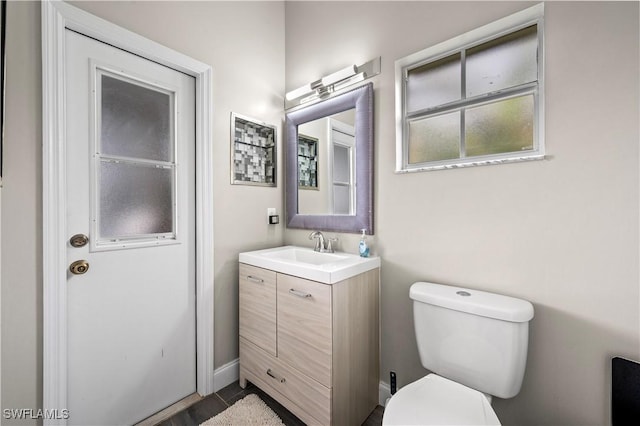 half bath featuring vanity, toilet, and baseboards