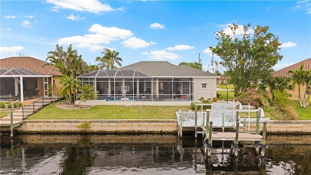 rear view of property with a water view, glass enclosure, a patio area, boat lift, and a lawn