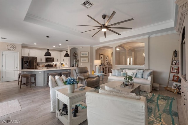 living room featuring crown molding, light hardwood / wood-style flooring, a raised ceiling, and ceiling fan