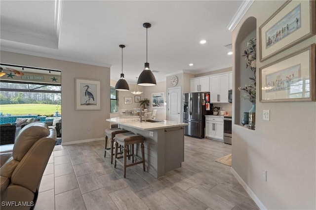 kitchen with crown molding, stainless steel appliances, an island with sink, white cabinets, and decorative light fixtures