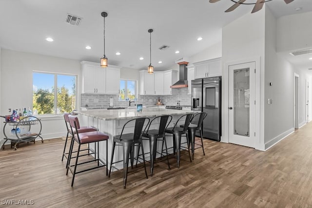 kitchen with white cabinets, stainless steel fridge, wall chimney exhaust hood, and a kitchen island