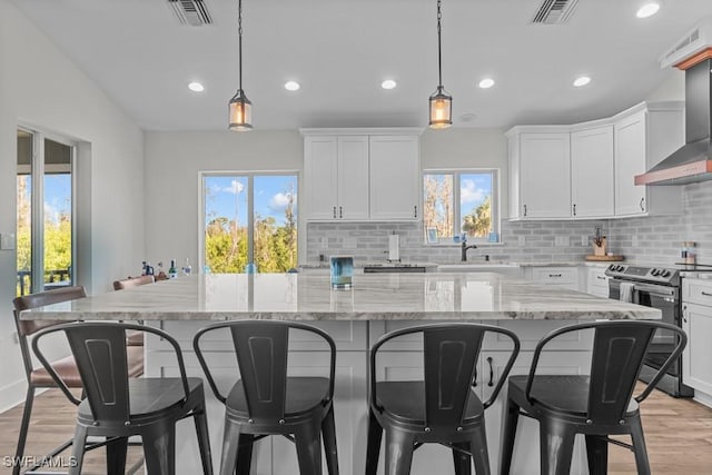 kitchen featuring pendant lighting, white cabinetry, a kitchen island, stainless steel electric stove, and wall chimney exhaust hood